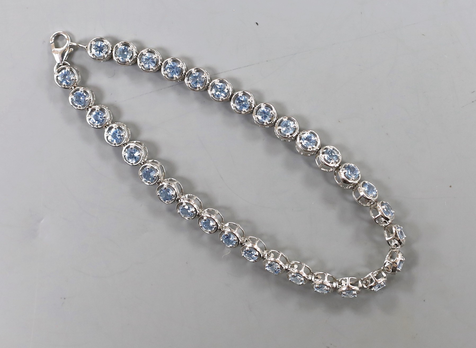 A modern 375 white metal and blue topaz line bracelet, 20cm, set with thirty two stones